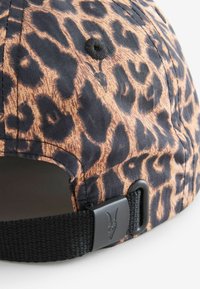 Casquette en imprimé léopard avec une sangle noire réglable, tissu texturé et un bouton de ventilation circulaire. La sangle est ornée d'une boucle en métal argenté.