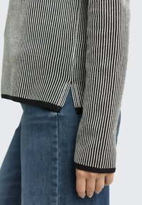 Czarny i biały sweter w paski z długimi rękawami, bocznymi szczelinami i prążkowaną teksturą, w połączeniu z niebieskimi dżinsami.