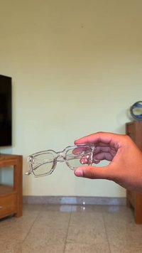 Óculos retangulares claros segurados à mão. Apresentam uma armação espessa e transparente, sem padrões ou detalhes visíveis. Textura suave.