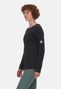 Svart långärmad tröja med rundad halsringning, med en logotyp på vänster ärm. Gjord av ett slätt material med minimala sömmar.