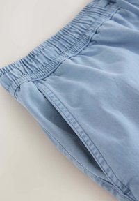 Pantalon à taille élastique bleu clair avec poche latérale visible et couture détaillée sur fond blanc.
