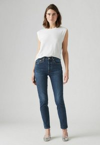 Witte mouwloze shirt gecombineerd met donkerblauwe high-waisted jeans en zilveren ballerina's, met een eenvoudig ontwerp en klassieke pasvorm.