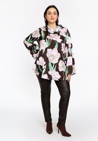 Vloeiende brown top met grote roze bloempatronen, gecombineerd met zwarte skinny faux leren broek en bruine hoge hakken.