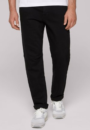 Black denim pants with a slim fit, featuring front pockets and a classic five-pocket design, paired with white athletic sneakers.