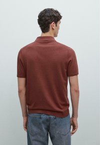 Hnědá polokošile s krátkým rukávem vyrobená z měkkého materiálu s klasickým límečkem. Disponuje přiléhavým střihem a žebrovaným lemem, v kombinaci se světle šedými džíny.