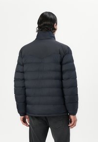 Navy puffer jacket with a high collar, quilted texture, and a curved seam detail at the shoulders. Lightweight material and fitted shape.
