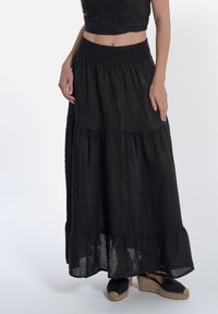 Zwarte linnen maxi rok met een smock tailleband, gelaagd ontwerp en een gerimpelde zoom. Gecombineerd met zwarte espadrilles.