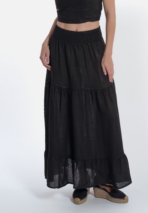 Zwarte linnen maxi rok met een smock tailleband, gelaagd ontwerp en een gerimpelde zoom. Gecombineerd met zwarte espadrilles.