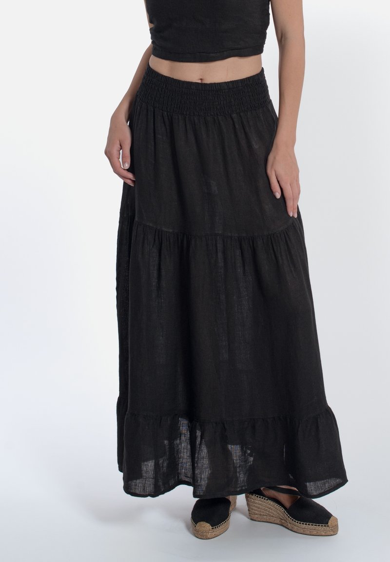 Zwarte linnen maxi rok met een smock tailleband, gelaagd ontwerp en een gerimpelde zoom. Gecombineerd met zwarte espadrilles.