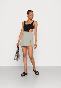 Bodysuit preto recortado emparelhado com uma mini saia cinza-claro com uma fenda lateral. A modelo segura uma bolsa com estampado de zebra em preto e branco.