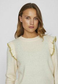 Sweter w kolorze kremowym z teksturowanym splotem, okrągłym dekoltem i falbaniastymi rękawami z złotymi akcentami. Miękka tkanina o swobodnym kroju.