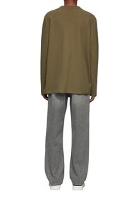 Olijfgroen long sleeve shirt met ronde hals en een relaxte fit, gecombineerd met lichtgrijze wijde broek en witte sneakers.