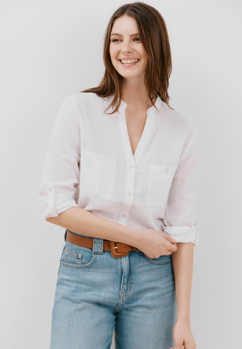 Witte linnen overhemd met opgerolde mouwen, met twee voorzakken. Gecombineerd met lichtblauwe denim jeans en een bruine riem.