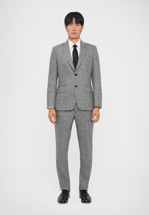 Abito grigio in lana con tessuto a trama, giacca monopetto, bottoni neri e pantaloni coordinati, abbinato a una camicia bianca e una cravatta nera.