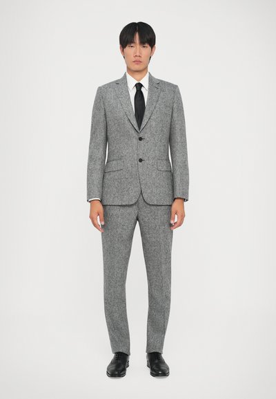 Costume en laine grise avec un tissu texturé, veste à boutonnage simple, boutons noirs, et pantalon assorti, porté avec une chemise blanche et une cravate noire.