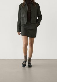 Szary teksturowany żakiet z dwoma przednimi kieszeniami, w zestawie z dopasowaną spódnicą. Uzupełniony czarnymi butami i brązowymi skarpetkami. Minimalistyczny design.