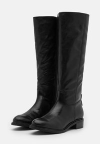 Botas de cuero negro hasta la rodilla con una textura suave, punta redonda, cremallera lateral y tacón bloque para estabilidad y soporte.