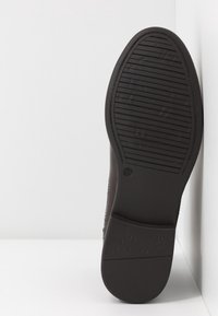 Suela de zapato marrón con goma texturizada para un mejor agarre, que presenta estrías y una impresión de logo. Bordes suaves que se estrechan hacia el talón.