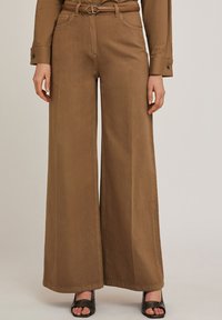 Wide-leg brown pants made of a textured fabric, featuring a high waist, belt loops, and large front pockets. Designed for a loose fit.