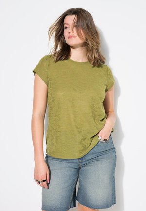 T-shirt vert olive à manches courtes avec une surface texturée, associé à des shorts en denim bleu clair. Le T-shirt a une coupe décontractée et un col rond.