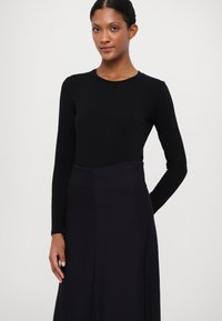 Mustapaitainen pitkähiha-asu, joka on yhdistetty tumman violetin, virtaavan hameen kanssa. Kangas näyttää sileältä, ja siinä on muotoiltu yläosa sekä löysä alaosa.