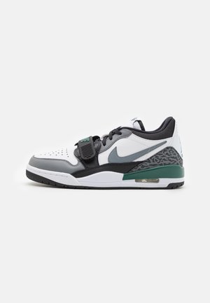 Basket de sport basse en blanc, noir et gris avec un accent vert, logo Nike, bride sur les lacets et détail au talon à motif.