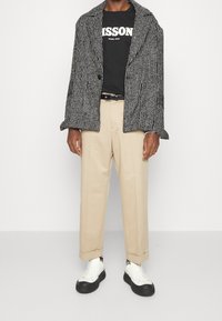 Svartvit randig oversized kavaj, svart t-shirt med vit tryck, beige skräddarsydda byxor och vita sneakers med svarta sulor.