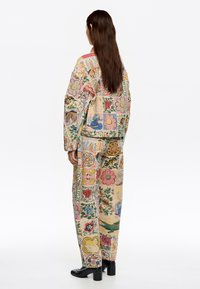Chaqueta y pantalones de patchwork en tela de algodón, con coloridos estampados florales y de animales, con mangas largas y corte relajado. Botas de tacón negras.