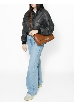 Femme portant une veste en cuir noire, un jean évasé bleu clair et des chaussures beige, portant un sac à bandoulière en cuir marron.