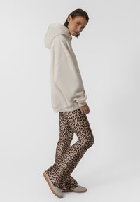 Bežinė oversized dydžio palaidinė su priekiu kišene, derinama su platėjančiais leggingais, išpuoštais rudos leopardo raštu, ir šviesių atspalvių avalyne.