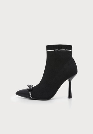 Μαύρο αστραγάλου με ψηλό τακούνι και μυτερή μύτη, πλεκτό ύφασμα, μικρός φιόγκος με λογότυπο μπροστά και κείμενο "KARL LAGERFELD" στο μανσέ και στον φιόγκο.
