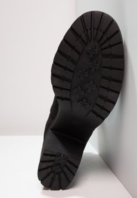 Černá podrážka boty se strukturou zaměřenou na přilnavost, s plochým, mírně vyvýšeným podpatkem. Gumový materiál s výrazným vzorem.