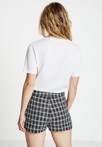 T-shirt blanc à manches courtes associé à un short en tweed noir et blanc avec un motif à carreaux et une taille élastique.