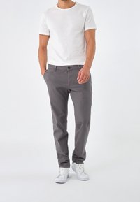 Pantalons en coton gris avec une coupe slim, dotés de poches latérales, d'une fermeture à bouton à l'avant, portés avec un t-shirt blanc à col rond et des baskets blanches.