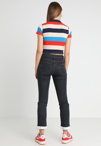 Polo de manga corta a rayas en rojo, azul, beige y marino, combinado con jeans de mezclilla negros y zapatillas rojas y blancas.