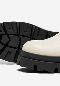 Stivali con suola spessa, caratterizzati da una parte superiore in crema liscia e una suola in gomma nera texturizzata con profonde scanalature per una migliore trazione.