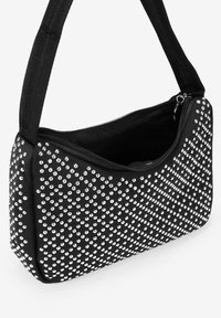 Bolso de mano negro con una superficie texturizada, que presenta tachuelas plateadas dispuestas en un patrón diagonal y un cierre con cremallera. Incluye una correa ajustable.
