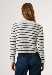 White and navy striped cropped sweater in textured knit; features a round neckline and fitted sleeves. Paired with dark denim trousers.