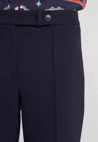 Námornické kalhoty s knoflíkovým zapínáním a předními kapsami, vyrobené z hladkého, strukturovaného materiálu s jemnými švy.