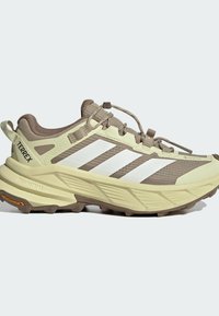 Light brown and beige hiking shoe with white stripes, thick sole with tread, quick-lace system, and "TERREX" branding on the heel.