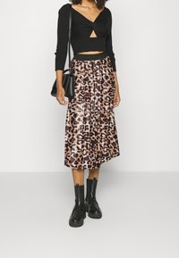 Top crop a maniche lunghe nero a coste con dettaglio anteriore attorcigliato, abbinato a una gonna midi plissettata con motivo a stampa leopardata e stivali neri chunky.