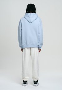 Sweat à capuche bleu clair, coupe décontractée, poignets et ourlet côtelés, associé à un pantalon de survêtement blanc et des baskets noires. Design minimaliste.