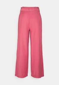 Pantalons rose à jambes larges avec une texture douce, une taille élastique et des plis subtils, fabriqués en tissu léger.