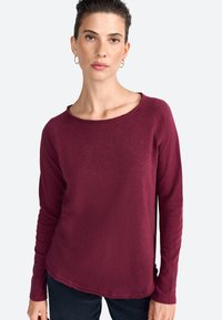 Burgundy pitkähihainen paita pehmeästä, teksturoidusta kankaasta, jonka pyöreä kaula-aukko ja raaka sauman koriste. Ominaisuuksina tiukasti istuvat hihat.