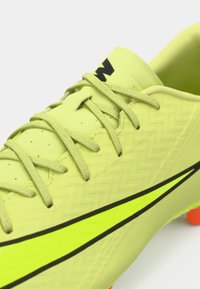 Zapatilla de fútbol amarilla neón con parte superior texturizada, acentos en negro y cordones. Presenta tacos naranjas en la suela para tracción y rendimiento.