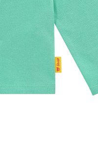 Turquoise langemouwen shirt van zacht katoen, met een label met de merknaam in het geel en een berenlogo. Glad van structuur, ribbelstof.