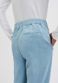 Pantalons en velours côtelé bleu clair avec une surface texturée, dotés d'une taille élastique et d'une poche au dos, présentés de profil.