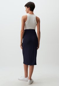 Top in cotone bianco a costine abbinato a una gonna midi texturizzata color navy, con silhouette aderente e sneakers bianchi.