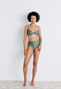 Tamsiai žalias bikini komplektas, apimantis liemenėlę su vielos palaikymu ir reguliuojamomis petnešėlėmis, derinamas su aukštu liemeniu. Švelni medžiaga su minimaliu dekoravimu.