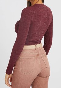 Bordeauxfarbene Langarmbluse aus strukturiertem Stoff, kombiniert mit hellrosa hochtaillierten Jeans mit Gesäßtaschen und beigem Bund.